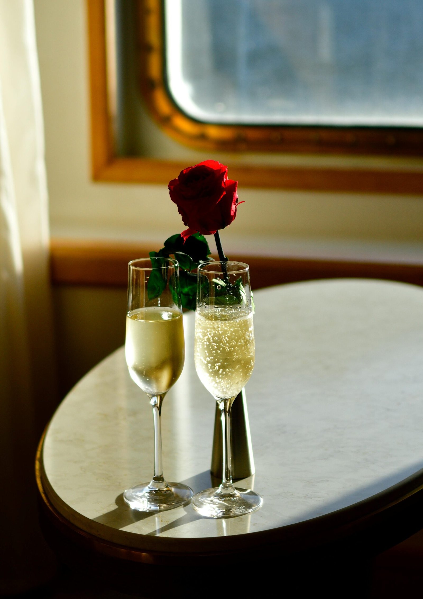 Elegant champagne glasses and a rose, illuminated by afternoon light on a cruise ship table.